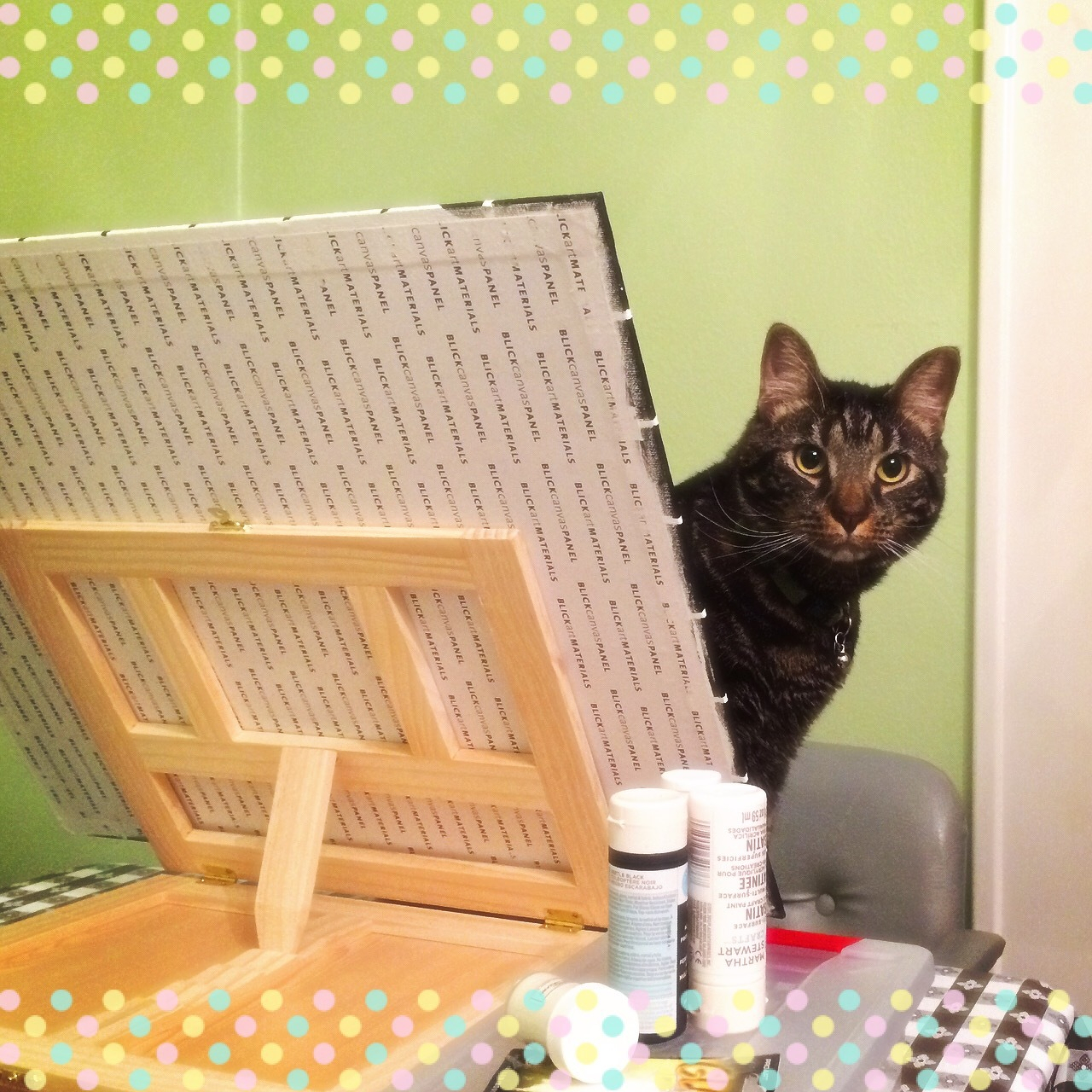 photo of a cat peaking around a canvas, which makes it look like he is the one working on the painting